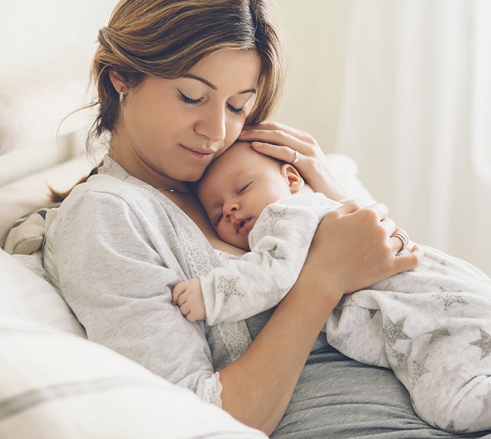 Mother holding sleeping baby after lip and tongue tie treatment