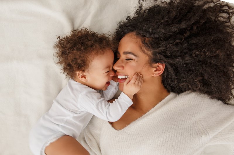 a mother and her baby lying on a bed laughing and playing together
