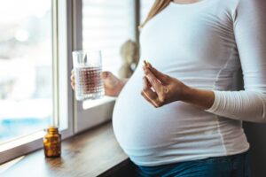 Pregnant woman holding glass of water and vitamin. 